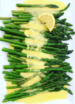 White plate with asparagus covered in a thick yellow hollandaise sauce.