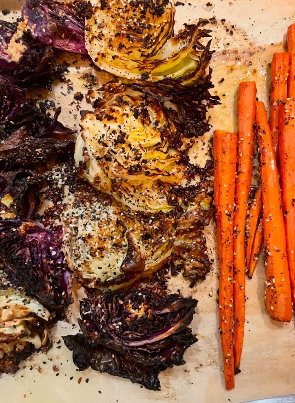 Baking sheet lined with parchment with large hunks of roasted cabbage and carrots.