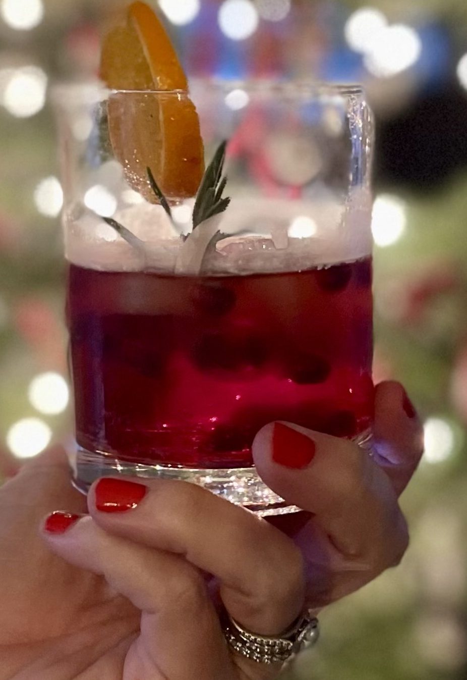 Womans hand holding a red cocktail in front of a Christmas tree.