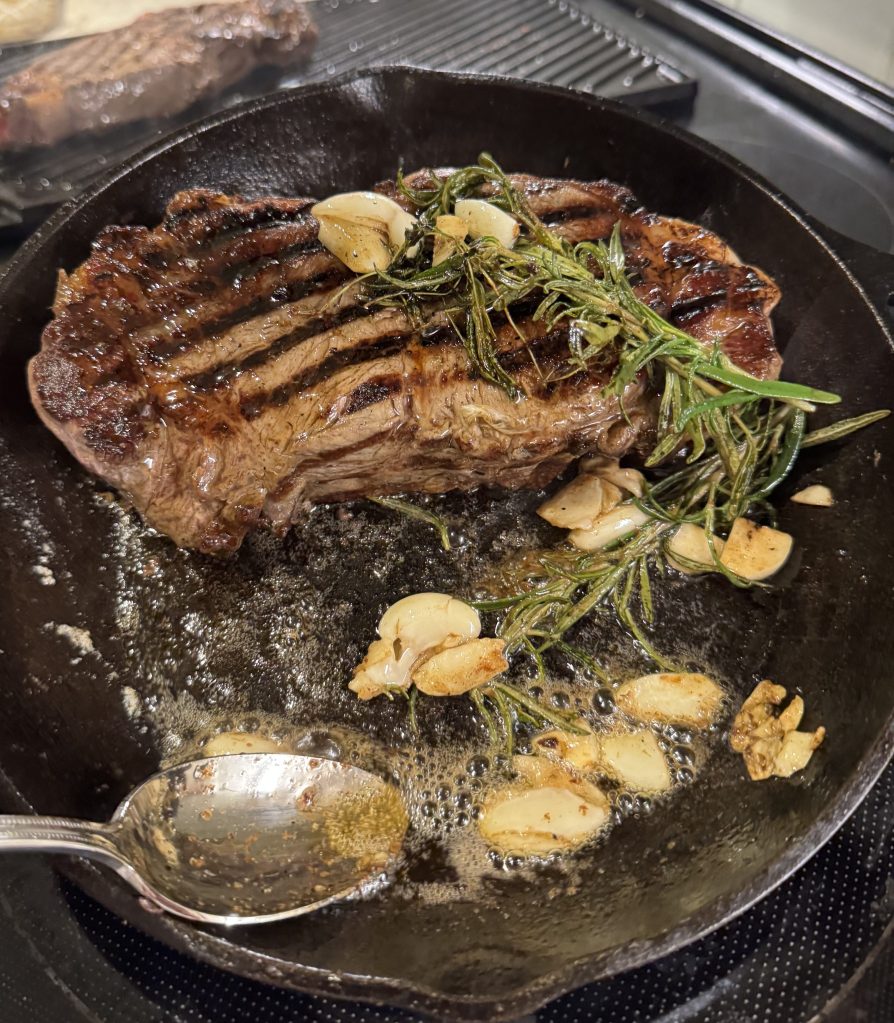 Steak cooking in a cast iron pan with garlic and rosemary.