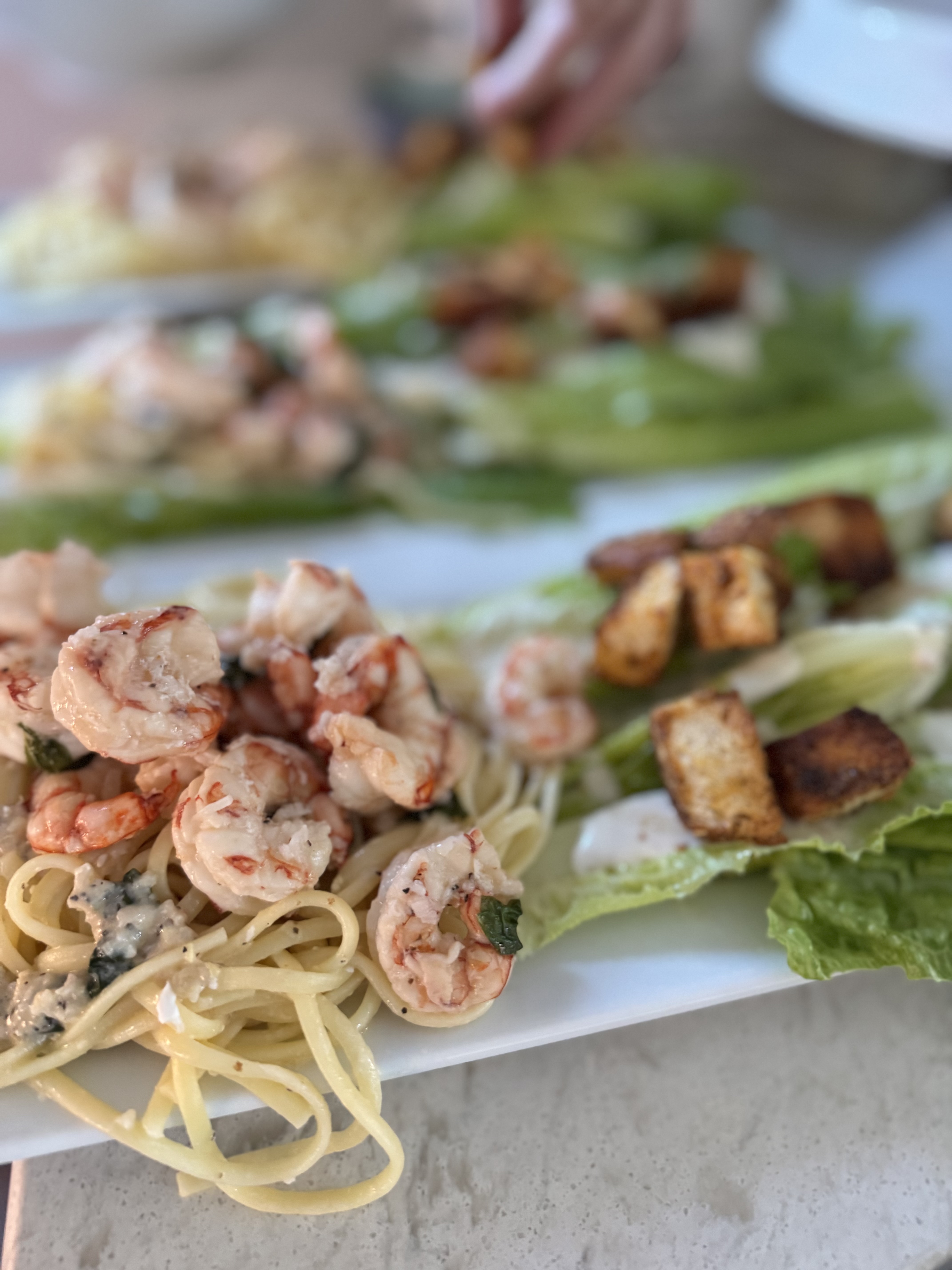 Sauteed shrimp with red peppers and pasta served beside a Caeser salad.
